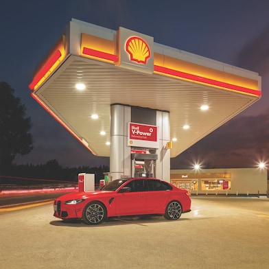 Červené auto stojící před tankovacím stojanem čerpací stanice Shell v nočních hodinách.