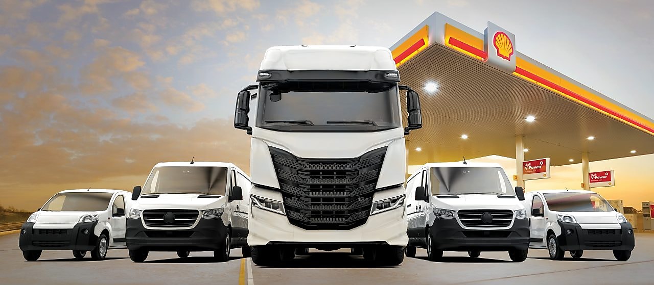 Bílá užitková vozidla, včetně nákladního auta a dodávek, zaparkovaná symetricky před stanicí Shell.