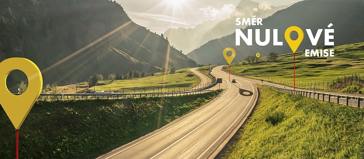 Sluncem zalitá silniční cesta mezi zalesněnými horami