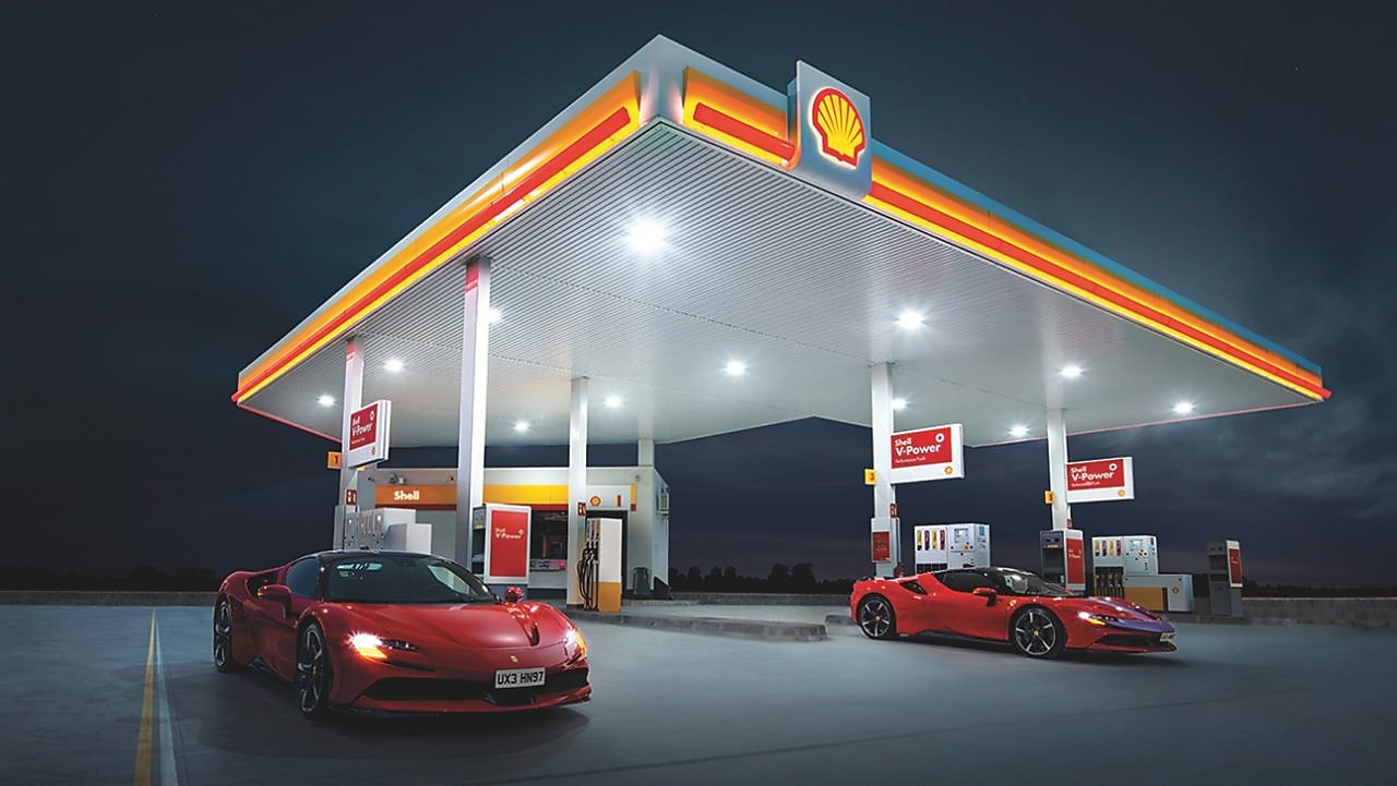 Obrázek čerpací stanice Shell v noci se dvěma zaparkovanými vozy Ferrari.