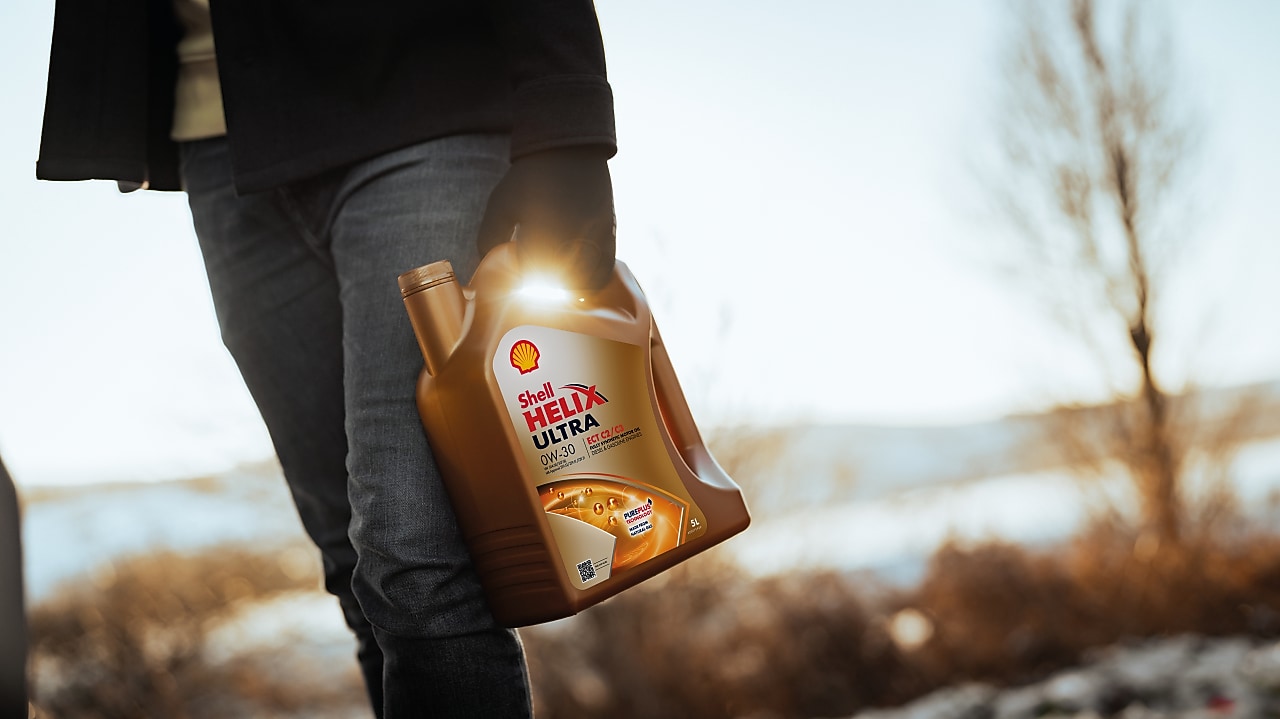 Ruka muže držícího olej Shell Helix Ultra.