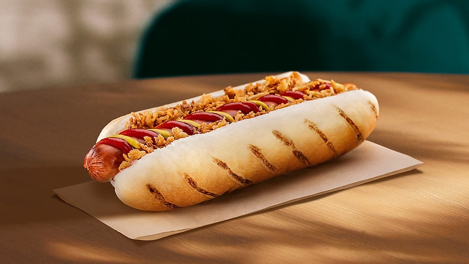 Na vizuálu lze vidět vegetariánskou nabídku hot dogu s hořčicí, kečupem a sušenou cibulí. 