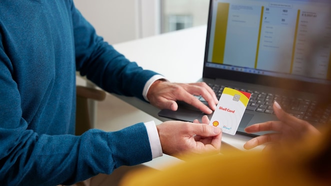 Detailní pohled na muže, který předává bílou čipovou kartu Shell Card ženě v kancelářském prostředí před notebookem