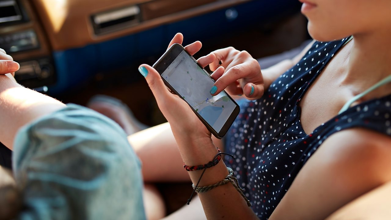 Foto muže a ženy v autě, jak se dívají na mapu v mobilu 