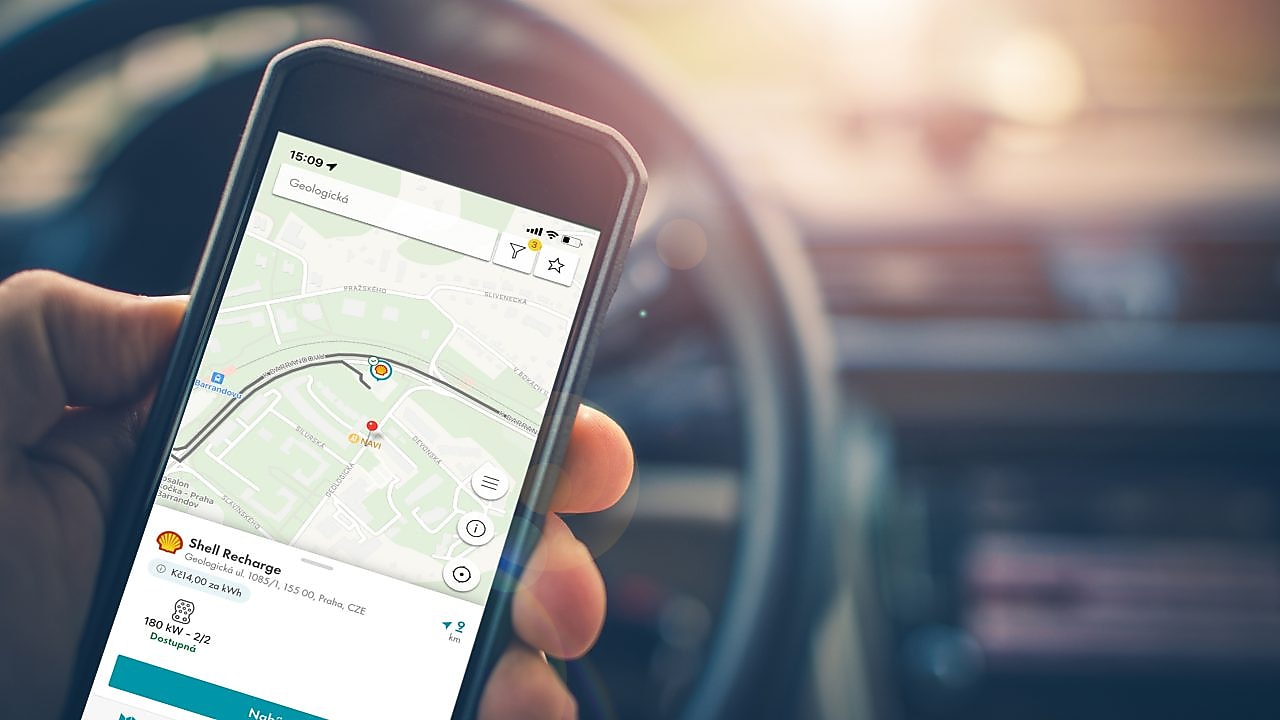 Ruka v autě drží mobil s Recharge aplikací s navigací k nejbližší stanici.