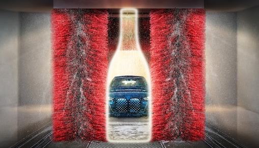 Na vizuálu vidíme výsek modrého auta v lahvi vína mezi kartáči mycí linky