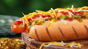 Foto hot dogu Mega s klobásou, karamelizovanou cibulkou, kečupem, hořčicí, sýrem a okurkovým relishem